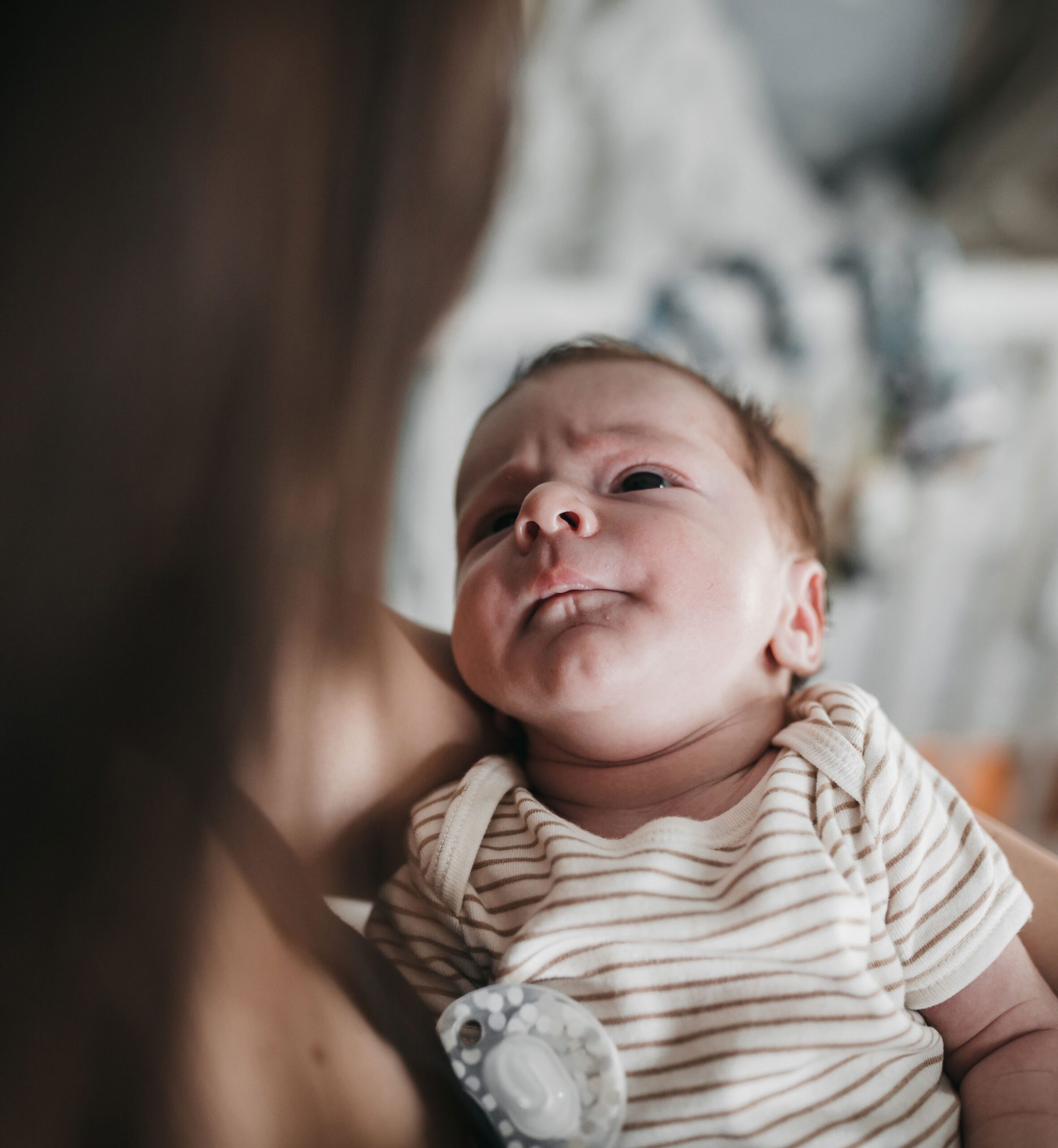 Newborn baby looking up while being held in mother&rsquo;s arms.
