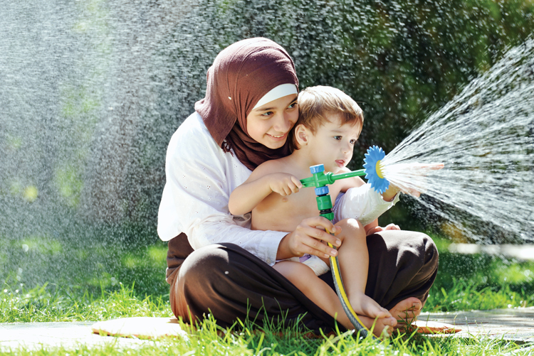 Adult and child playing with a garden hose outdoors.