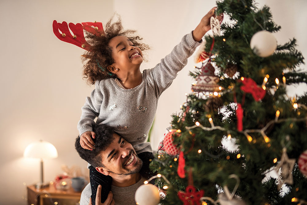 Child decorating Christmas tree on adults shoulders, smiling
