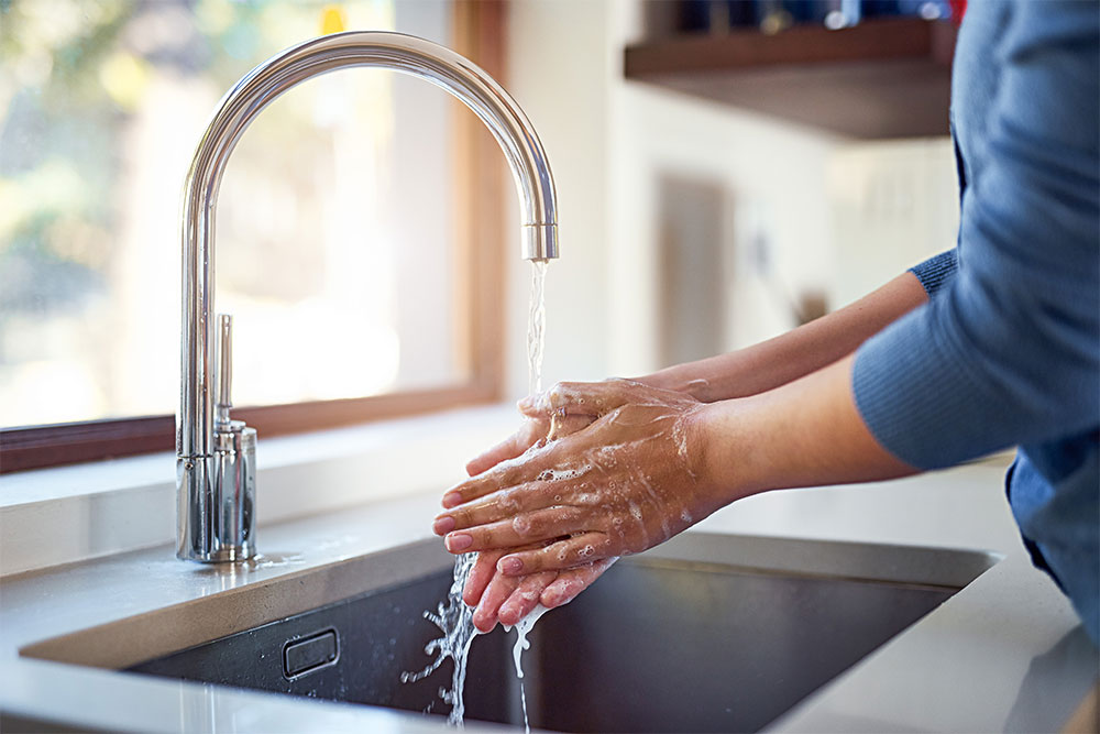 Hands washing under running kitchen faucet