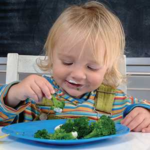 Child happily eating broccoli at the table
