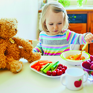 Toddler enjoys soup with colorful vegetables nearby