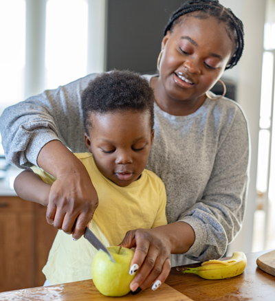 Child and adult slicing apple together in kitchen