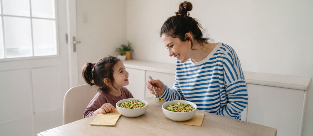 Mother feeding daughter a healthy meal at kitchen table