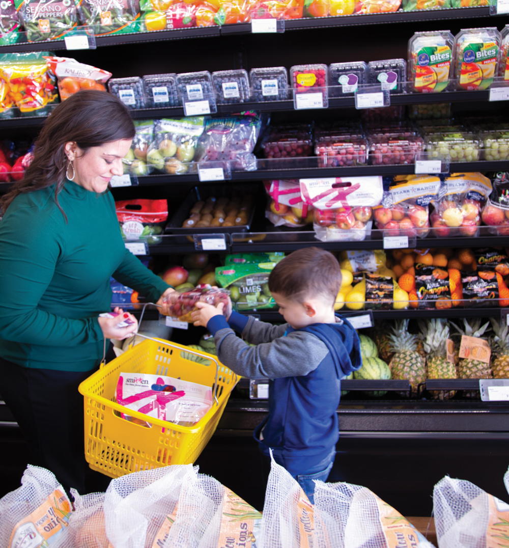 Adult and child grocery shopping together, holding grapes.