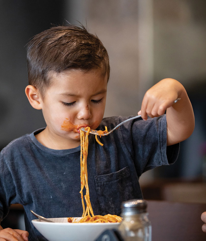 Child eating spaghetti with fork enthusiastically.